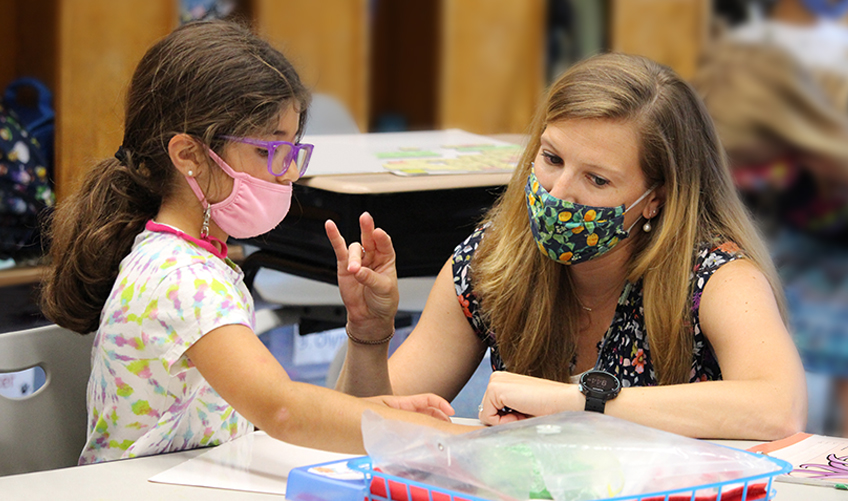 A masked teacher and student tapping out letter tiles